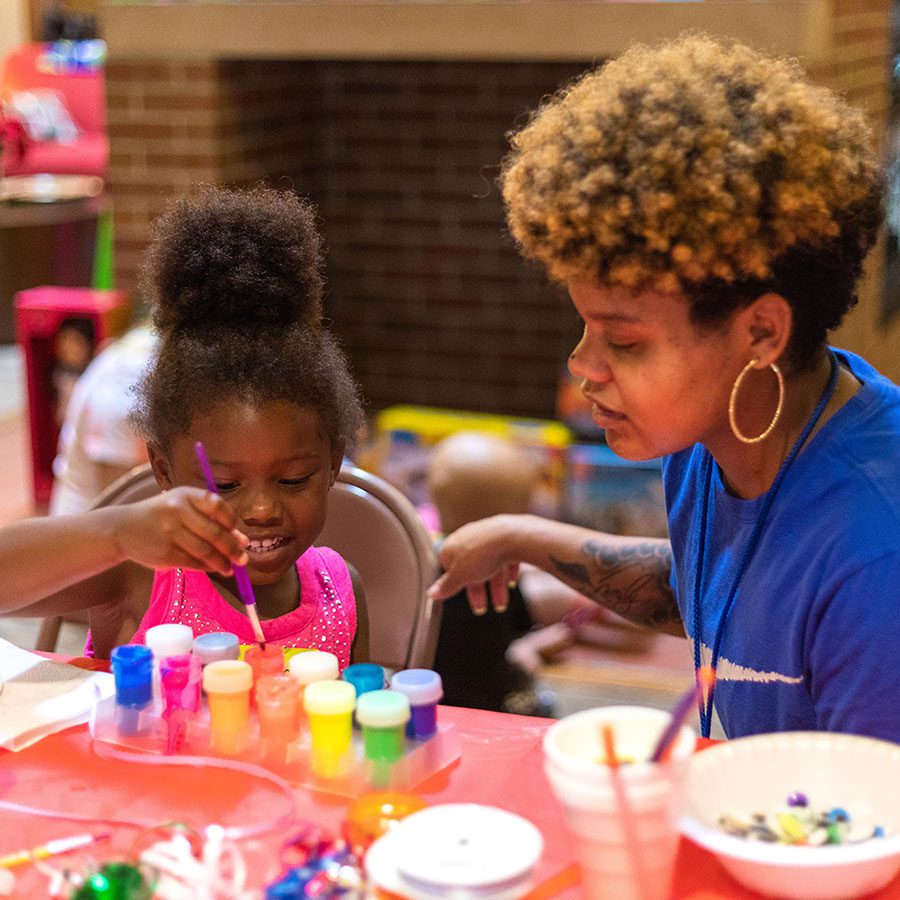 child and volunteer painting at christmas in july event